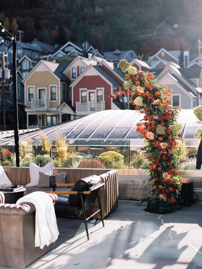 Rooftop lounge setup with a bold fall floral installation, cozy seating and colorful Park City buildings in the background.