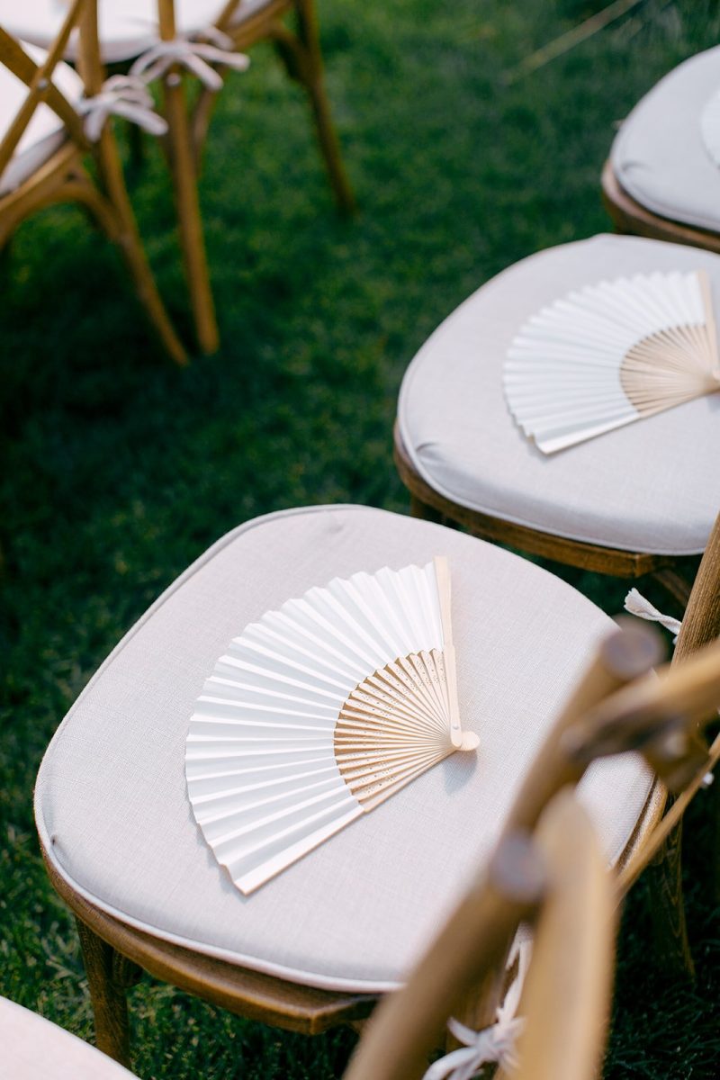 Close-up of white paper fans placed on cushioned wooden wedding chairs for an outdoor summer wedding ceremony in at 4U Ranch in Utah.