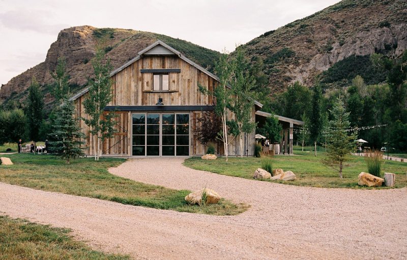 Rustic wooden barn wedding venue surrounded by greenery, gravel pathways and rocky Utah canyon views.